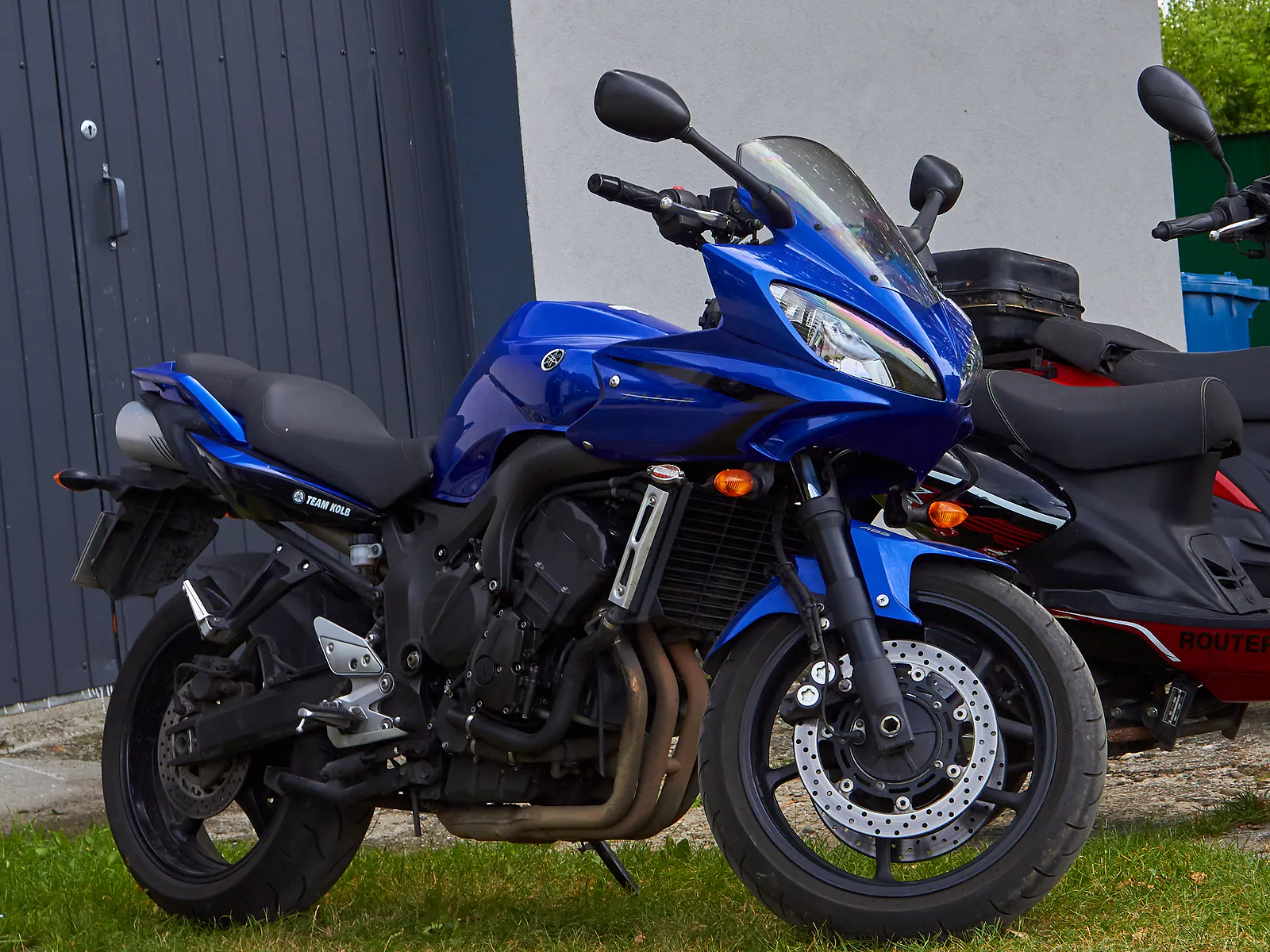 Niebieska Yamaha FZ6 zaparkowana na trawie przed warsztatem Motofil, obok skuter czekający na serwis